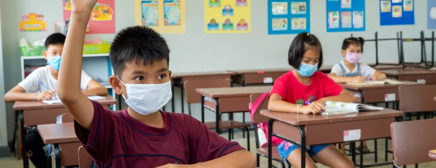 School kids wearing protective mask to Protect Against Covid 19,Group of school kids with teacher sitting in classroom and raising hands,Elementary school,Learning and people concept.