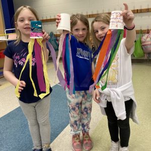 Three elementary-age girls holding up an art project.