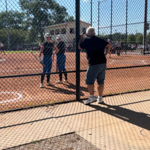 Bus drive Mike Trude talking to two NWHS Wolves softball players by the fence.