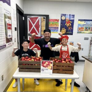 Two Sugar Creek Elementary students and one nutrition staff member serving apples while flexing their bicep muscles.