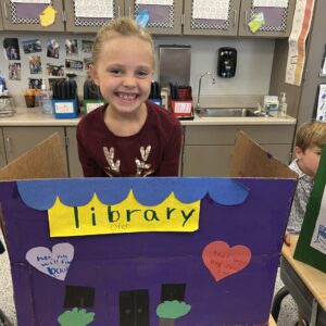 Student standing behind her cardboard creation she made for the classroom social studies project.