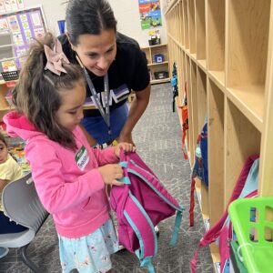 Staff member helping preschool student with her backpack.