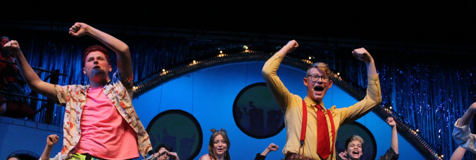 Bikini Bottom stage full with vibrant colors and costumes. Actors make a horseshoe shape above their heads.