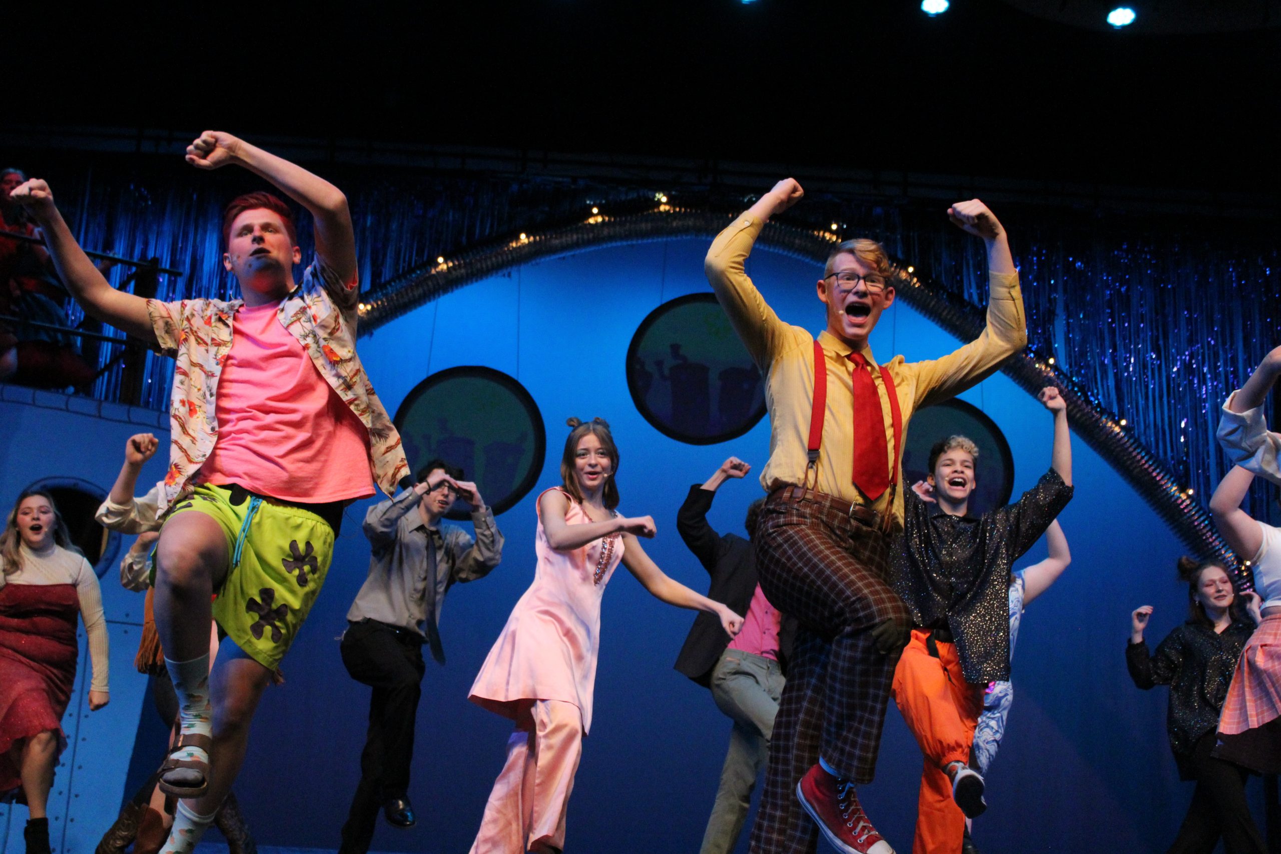 Bikini Bottom stage full with vibrant colors and costumes. Actors make a horseshoe shape above their heads.